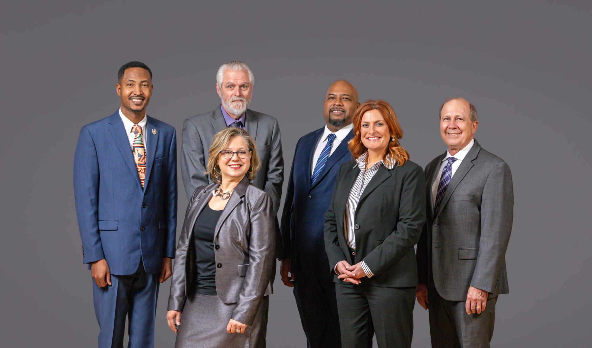 Group photo of the entire Board of Commissioners standing in a group with a gray background